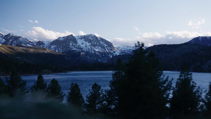 Driving past a majestic, snow-capped mountain range and a beautiful blue lake at golden hour