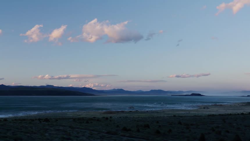 A beautiful sunset view of a large lake with distant mountains, seen from the window of a moving car