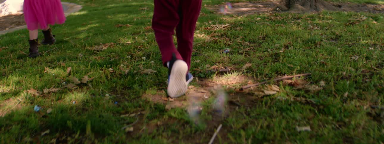 Close up slow motion shot of a toddler's feet walking through grass as soap bubbles float down