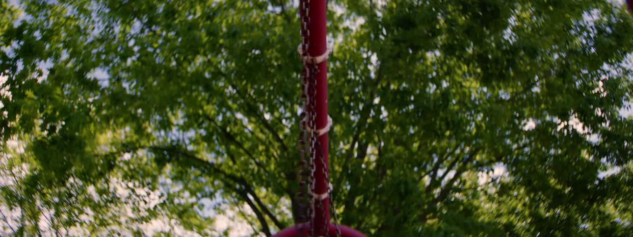 Low angle shot of an empty red swing gently swaying back and forth in a park on a sunny day