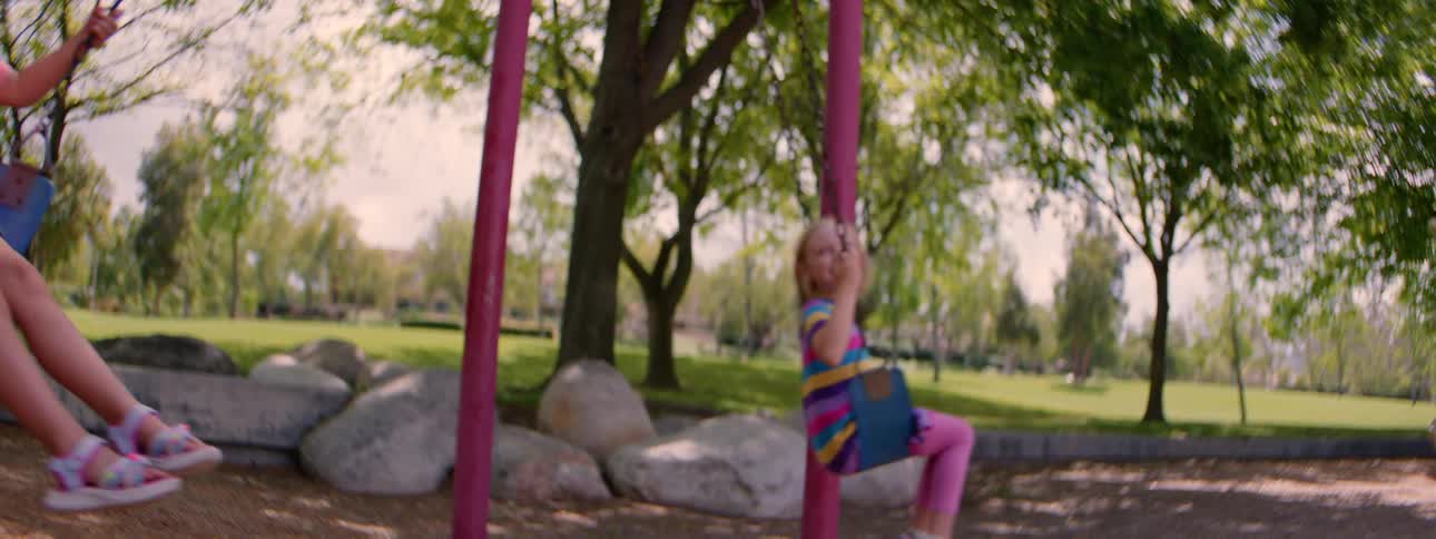 Two happy young girls have fun swinging together at a park playground in slow motion