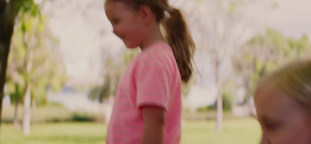 Close-up slow-motion shot of two adorable little girls smiling and holding hands as they walk together in a park