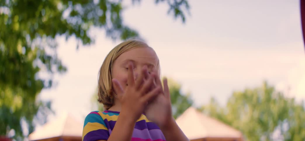A joyful young girl claps her hands and then holds them up to the camera with a big smile while playing outside