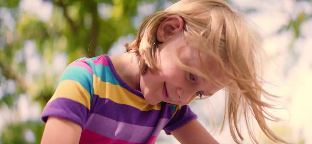 Slow motion close-up of a happy little blonde girl in a striped shirt, her hair blowing in the breeze as she plays outside