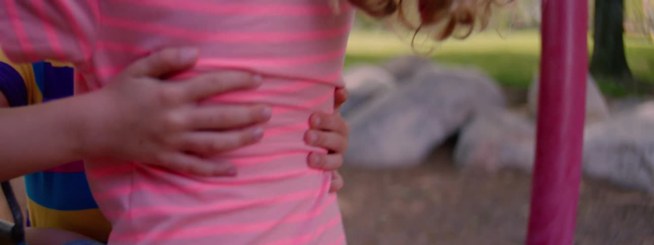 Close-up shot of a young girl in a pink striped shirt hugging a friend at a park playground