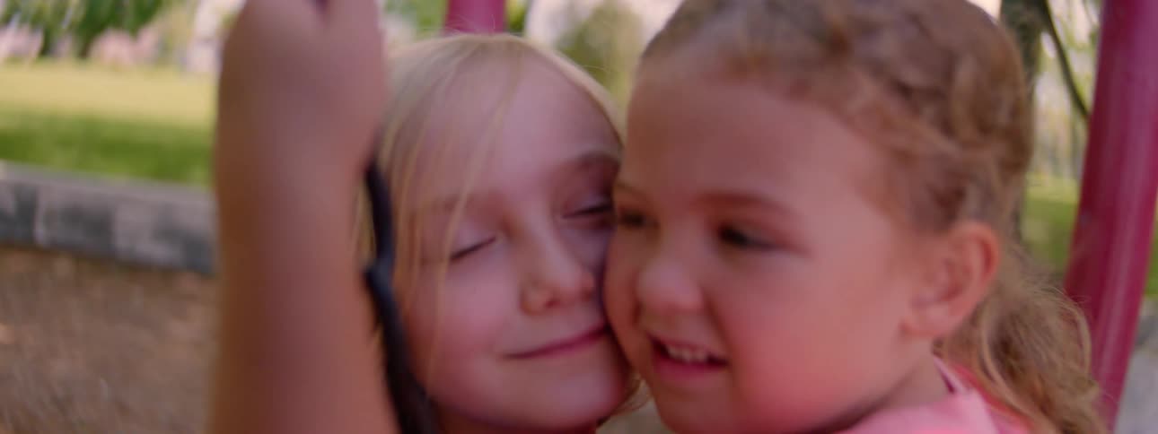 Close up of two young sisters sharing a tender moment, hugging on a swing in slow motion