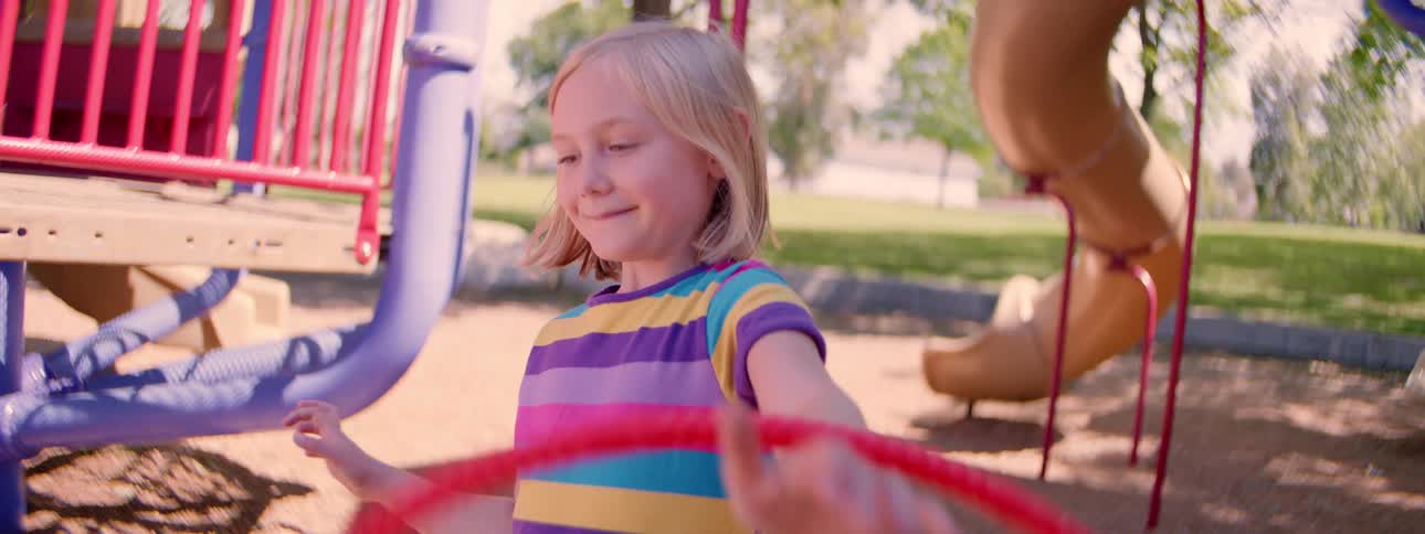 Slow motion of a smiling young girl in a colorful shirt playing with a red rope at the playground before making a funny face