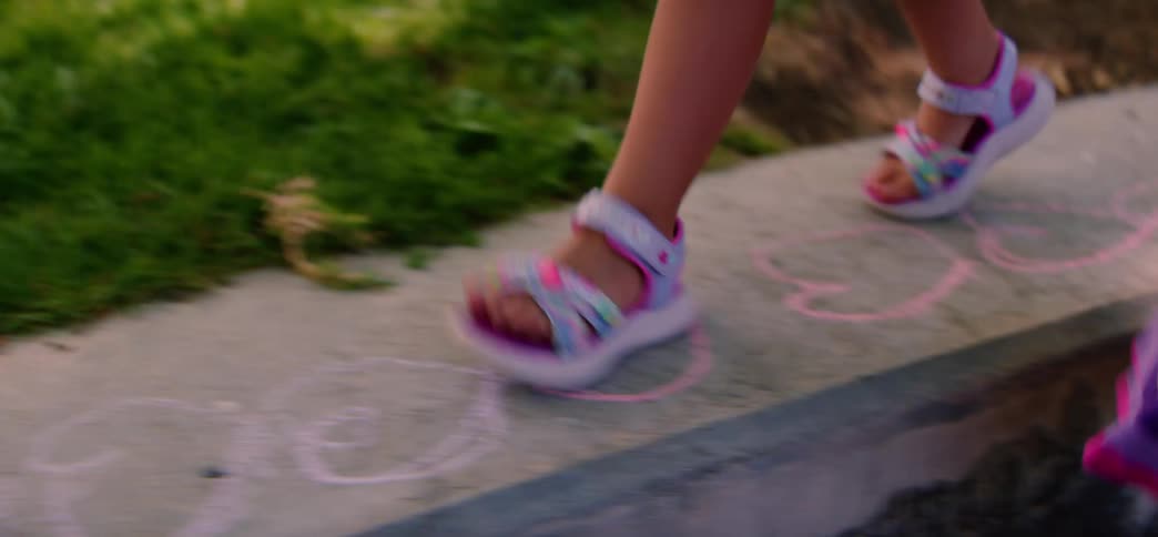 A young girl in colorful sandals balances on a stone ledge decorated with chalk drawings while holding a hand for support