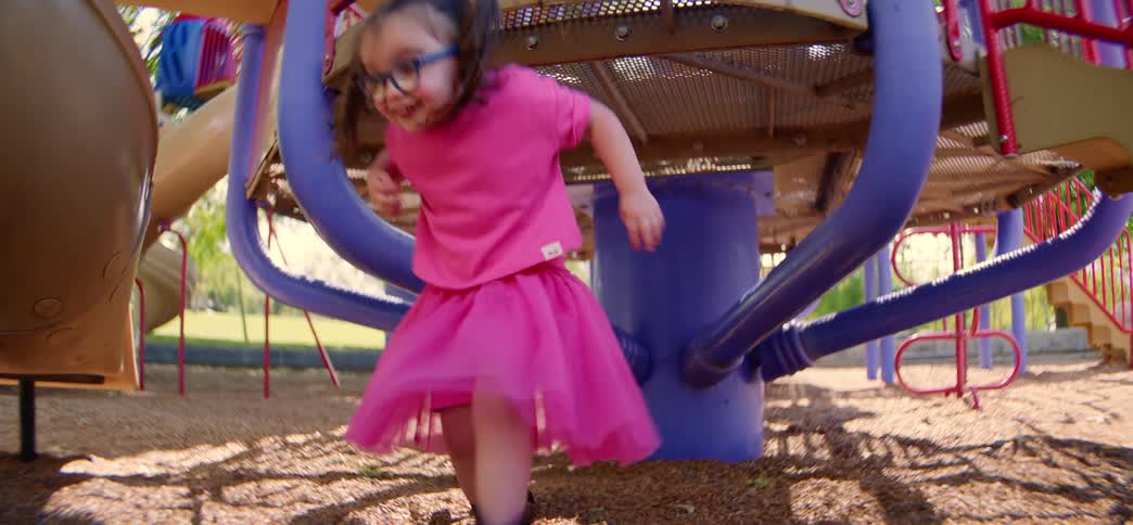 Slow motion shot of three diverse little girls playing together under playground equipment on a sunny day