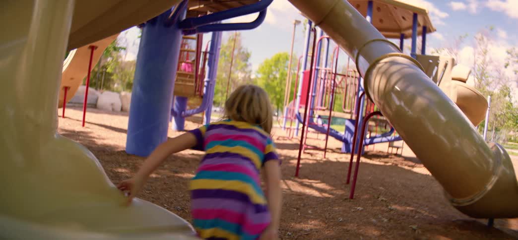 Slow motion shot of a smiling little girl sliding down a spiral playground slide on a sunny day