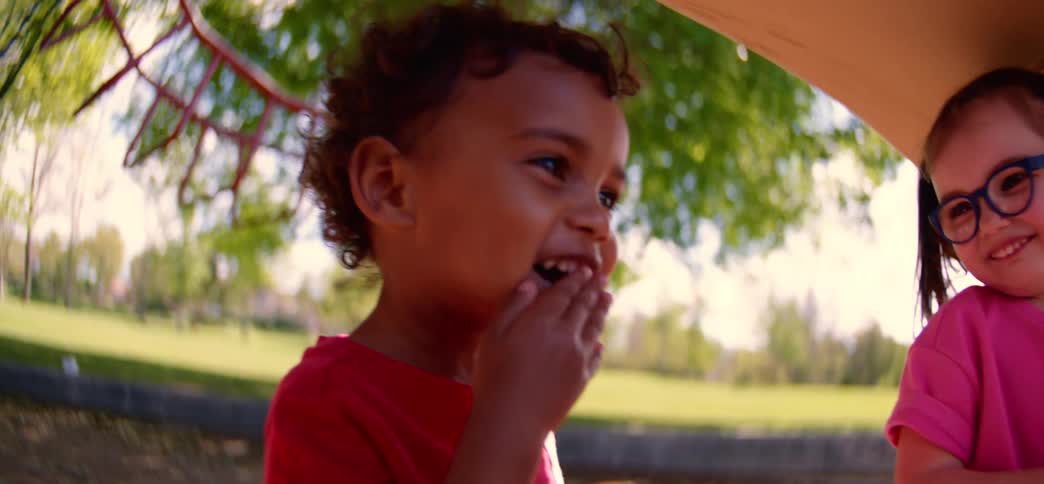 Two happy toddlers, a boy and a girl, play together at the playground on a sunny day in slow motion