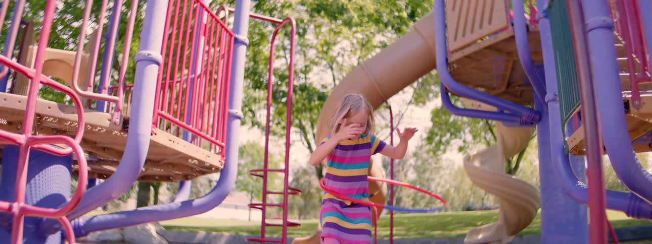 A joyful young girl in a colorful striped dress happily hula hoops in slow motion at the playground