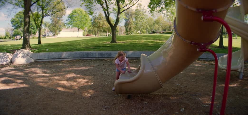 A little girl in slow motion laughing and playing while trying to climb up a playground slide