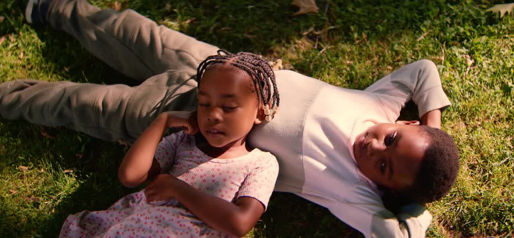 A high-angle view of a young brother and sister relaxing together, lying on the green grass on a sunny day