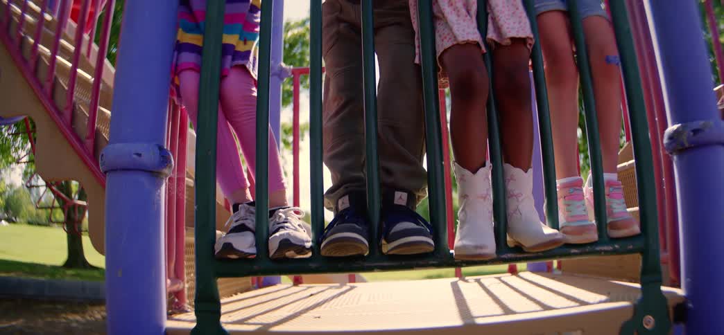 A low-angle shot tilts up from the feet to the smiling faces of a diverse group of young friends on a playground