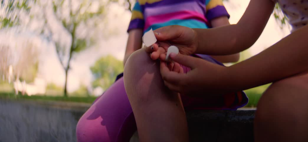 Close-up of a child's hands carefully applying a colorful floral bandage to another child's knee