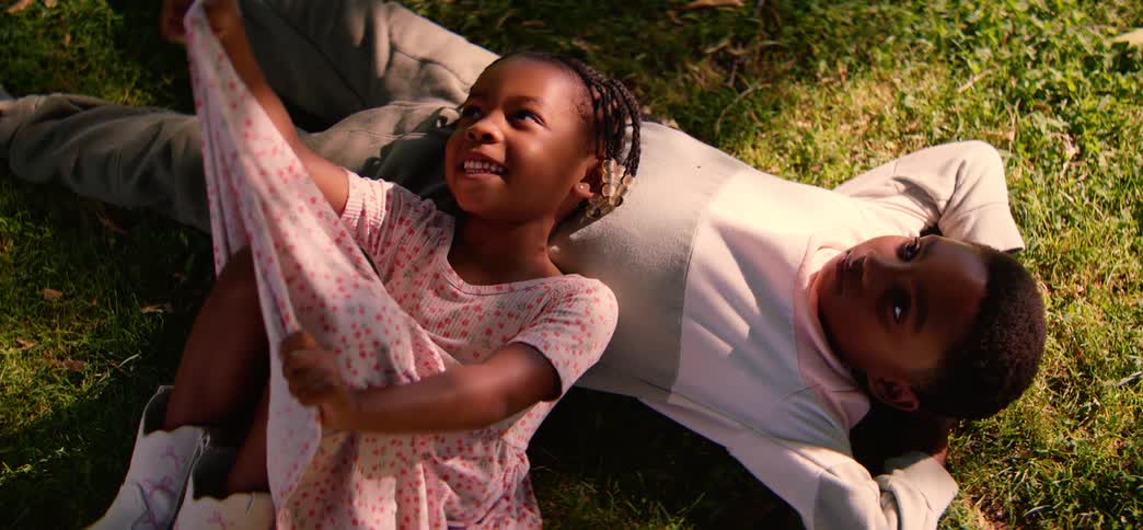 A happy little girl and her brother relax together in the sun-dappled grass on a beautiful day
