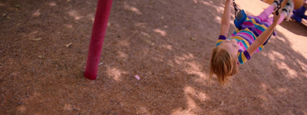 Point-of-view shot of a happy young girl smiling as she swings back and forth in slow motion at the park