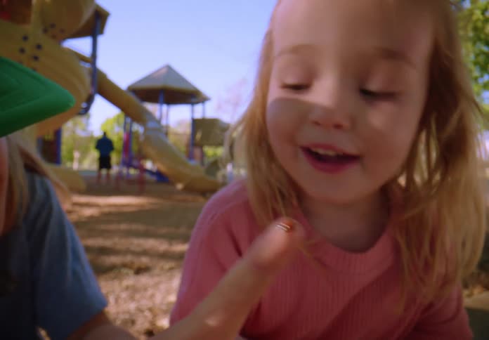 A curious little girl smiles as she watches a ladybug crawl on a finger at the playground