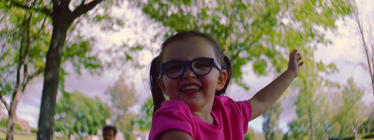 Close-up slow motion of a delighted young girl with glasses and pigtails trying to catch bubbles outdoors