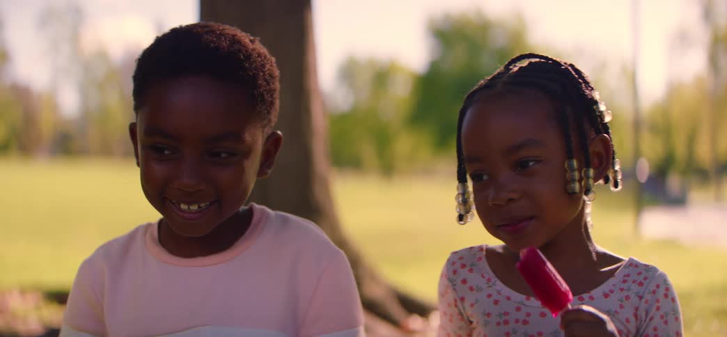 A slow-motion close-up of a brother and sister enjoying popsicles with their pet dog in a sunny park