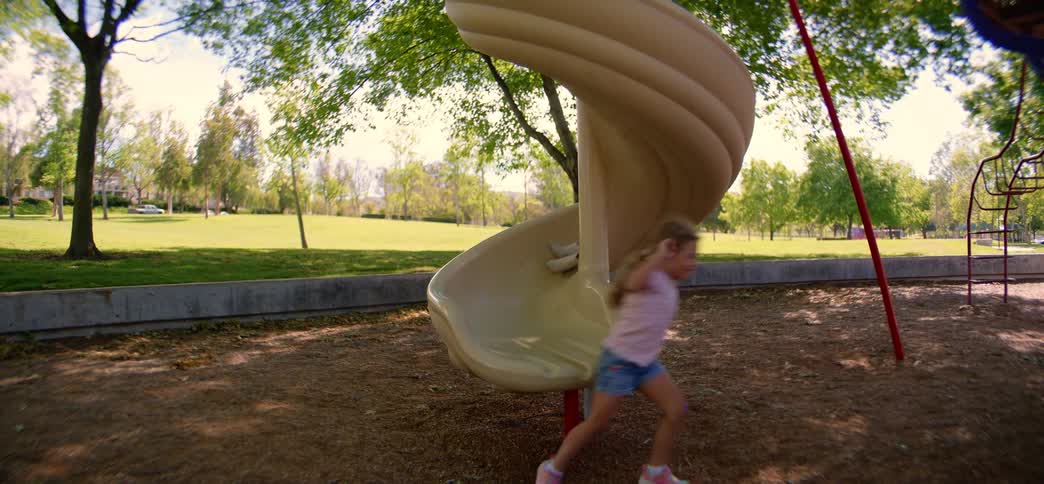 Slow motion wide-angle shot of a diverse group of children taking turns going down a spiral slide at a park playground