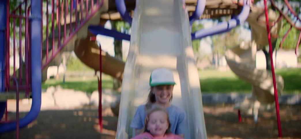 Slow motion shot of two happy sisters sliding down a playground slide together on a sunny day