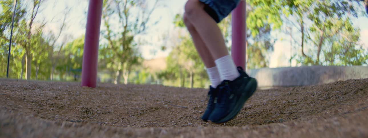 A slow-motion, low-angle shot captures a child's feet dangling and swinging back and forth on a playground swing