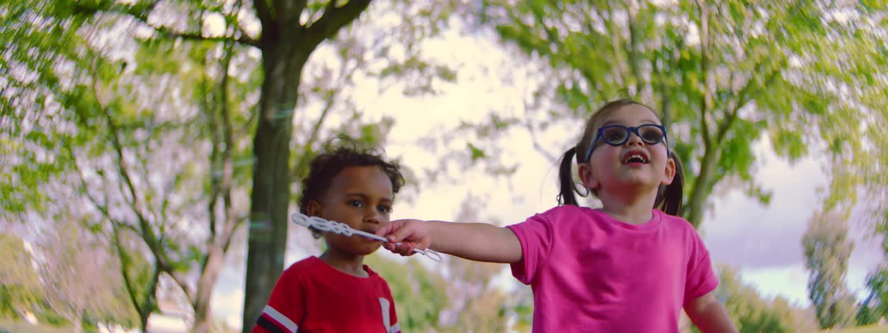 Slow motion shot of two adorable toddlers playing together and blowing bubbles with a bubble wand in a sunlit park