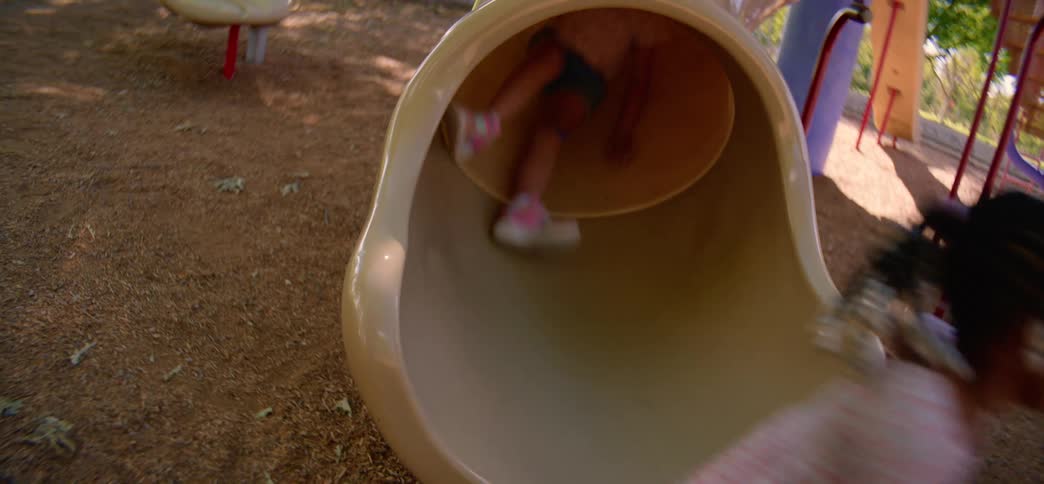 POV from the bottom of a slide as several happy kids come down the tube in slow motion