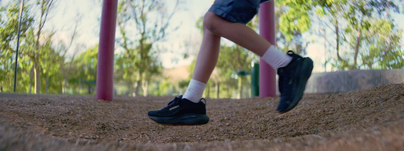 A slow-motion close-up of a child's feet in sneakers as they swing back and forth on a swing set at a sunny park playground
