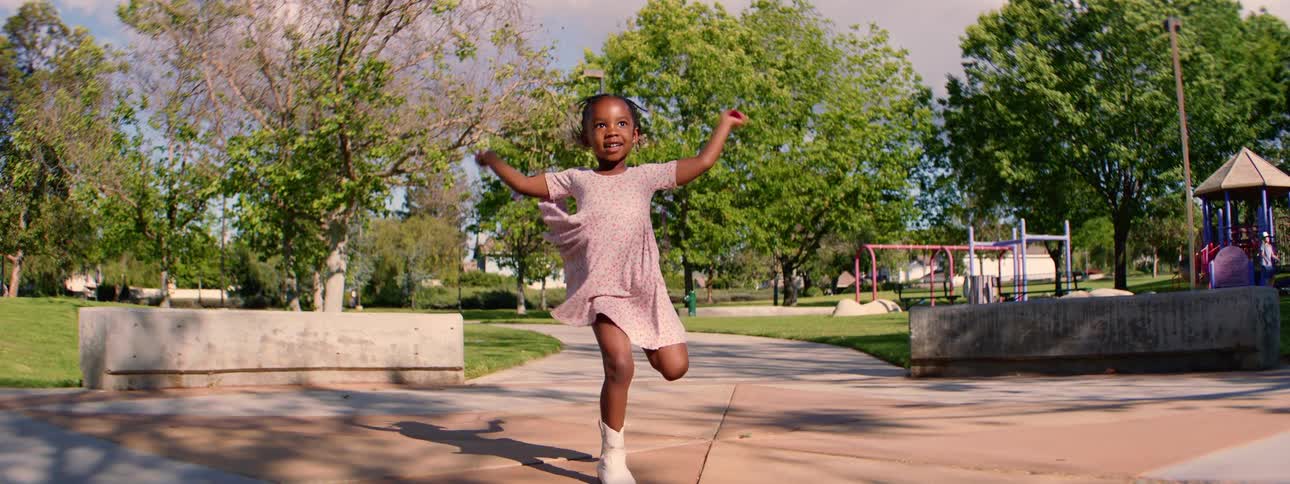 An adorable young girl in a pretty dress and boots smiles as she jumps rope in super slow motion at the park on a sunny day