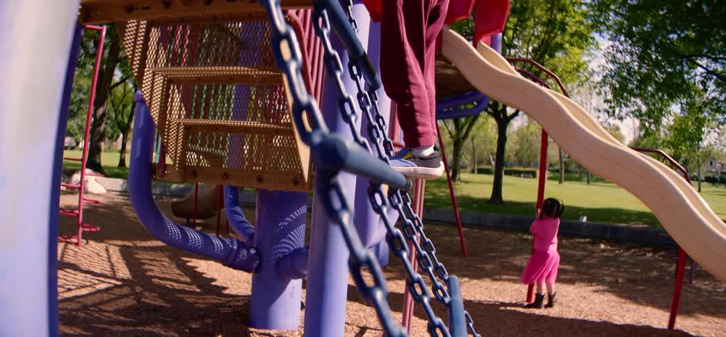 Slow motion shot of a happy young boy conquering a chain ladder at a park playground on a sunny day