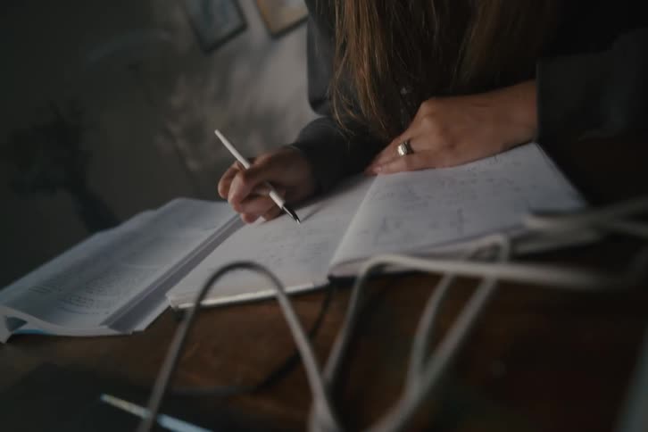 Close-up shot tilts down from a dedicated student's face to her hand as she writes notes in a dimly lit room