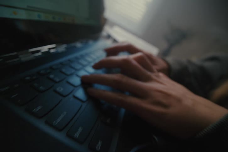 Extreme close-up of hands typing on a laptop keyboard, pulling out to reveal a high-tech computer motherboard on a desk