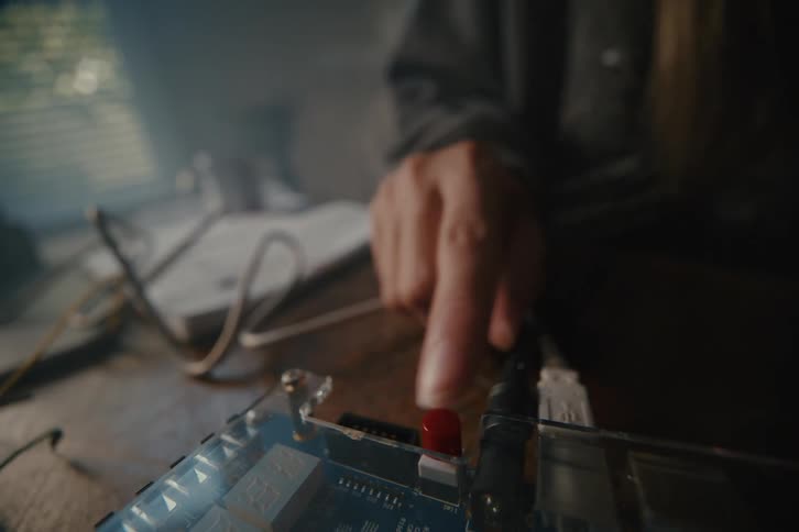 A tense close-up shows a finger pressing a red button, activating a digital countdown timer on a mysterious electronic device