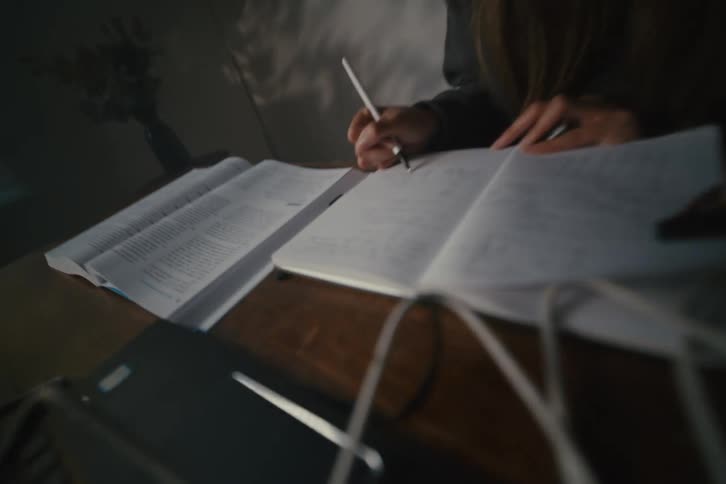 A focused female STEM student diligently studies late into the night, writing in her notebook at her desk