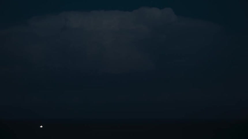 A powerful thunderstorm erupts with dramatic flashes of lightning inside a massive cloud over the ocean at night