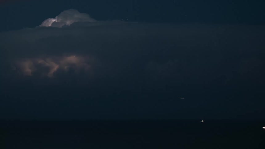A dramatic timelapse shows a powerful electrical storm brewing over the ocean with constant lightning flashes illuminating the dark clouds from within