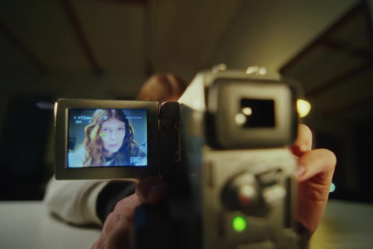 Close-up shot of a vintage camcorder recording a woman's face on the flip-out screen