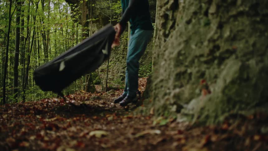A climber tosses down a bouldering crash pad in a lush forest in super slow motion as autumn leaves fall