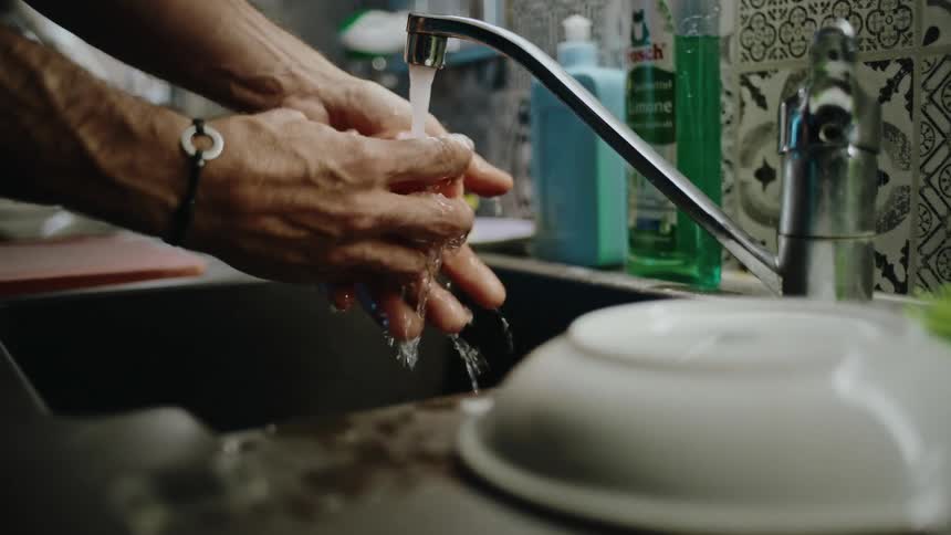 A man's hands carefully wash a fresh apple under running water from a kitchen tap in slow motion