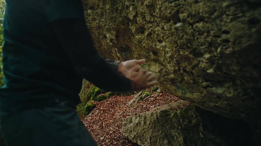 A male climber in a green shirt chalks his hands in preparation for bouldering in the forest