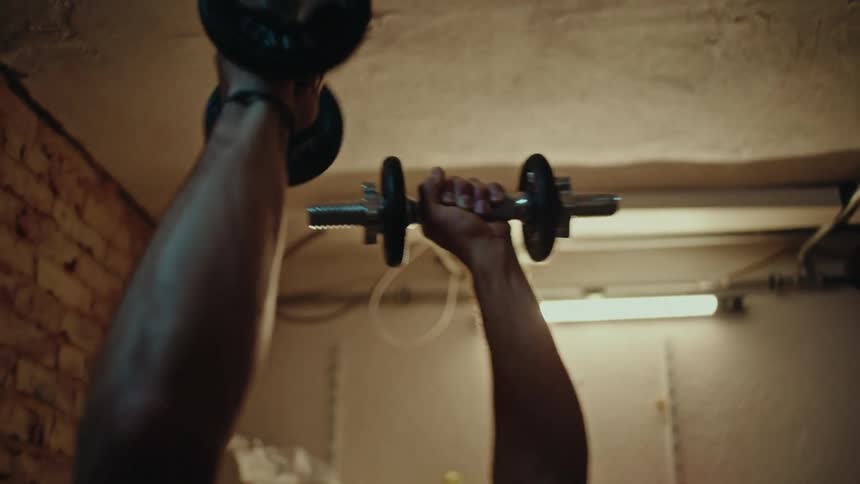A determined man with glasses performs a dumbbell chest press in a gritty, makeshift home gym in his basement