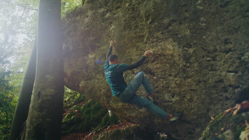 A strong male climber successfully completes a challenging bouldering route on a large rock in a beautiful sun-dappled forest