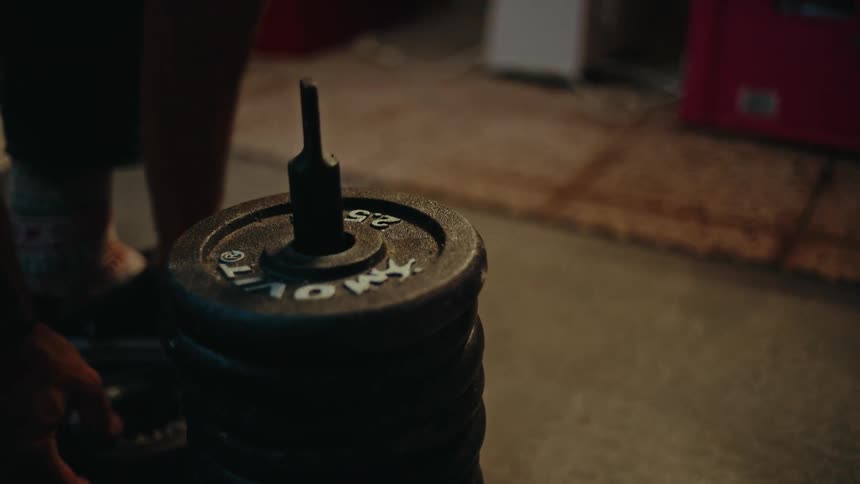 A person stacks several weight plates on a dumbbell in a home gym in slow motion