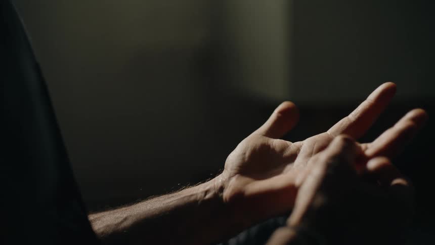 A dramatic slow motion close-up of a man's expressive hands opening, closing, and gesturing in a dark room