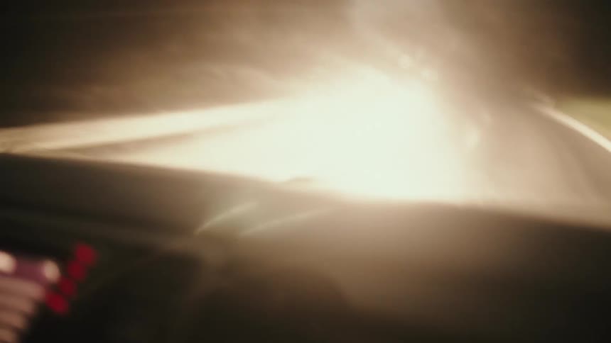 A disorienting and blurry point-of-view from inside a car driving on a dark, winding road through a foggy forest at night