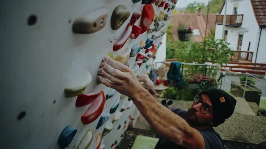 Focused male climber in a beanie trains on an outdoor artificial bouldering wall in slow motion
