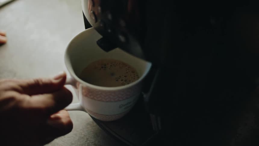 A person takes a freshly brewed cup of coffee from an automatic espresso machine
